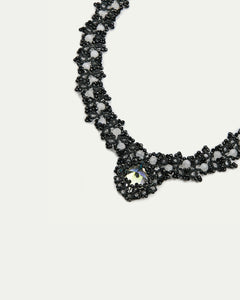 Black beaded Margueritte necklace, intricate lattice pattern with reflective central gem, elegant side view.