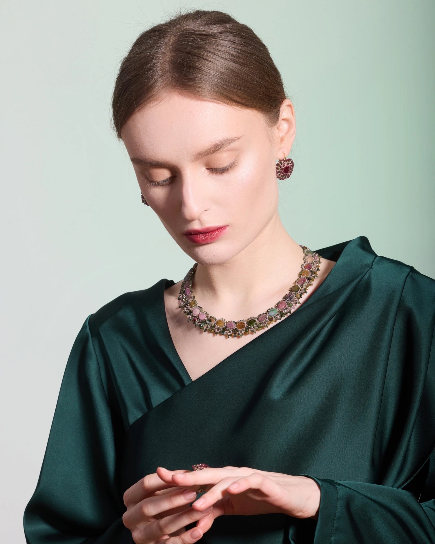 Multicolor gemstone necklace in a floral pattern, worn with matching earrings and a dark green satin dress.