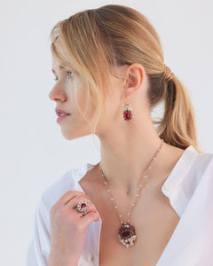 Red NAYA RING in size 53, gold-tone metal, intricate gemstone setting, side view, worn with matching earrings and necklace.