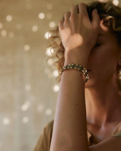 Gold silk bracelet with freshwater pearls and garnet details worn on wrist.