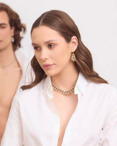 Gold-tone Paige Necklace with intricate design, worn by model in white shirt, showcasing side angle and clasp detail.