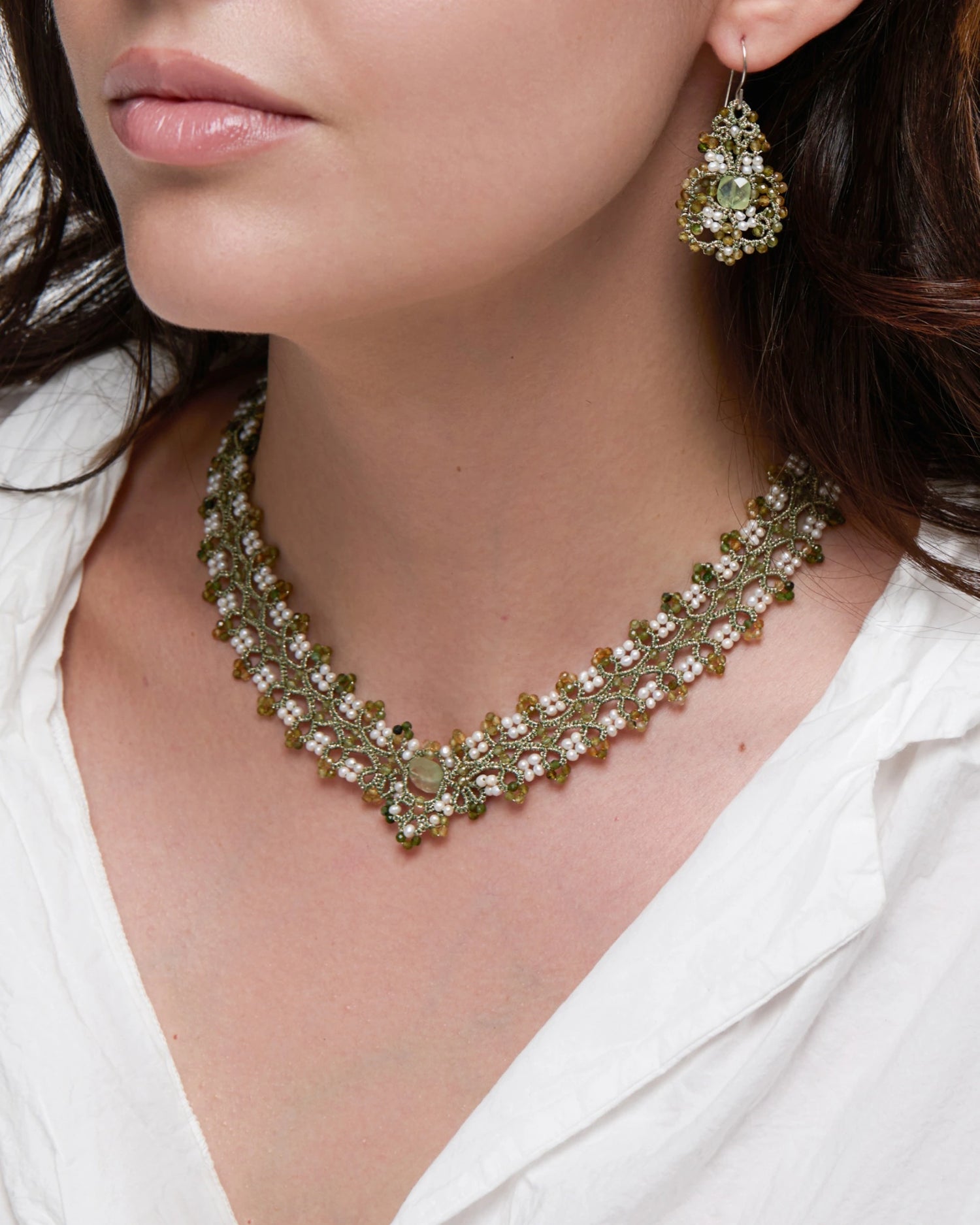 Green PAIGE necklace with silk, freshwater pearls, and tourmaline detailing, worn by a person in white shirt.