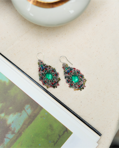 Green Pamela earrings with intricate beaded design, featuring multicolored stones on a light fabric background.
