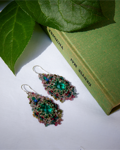 Green silk earrings with pearl, crystal, sapphire, emerald detailing, set against a close-up textured background.