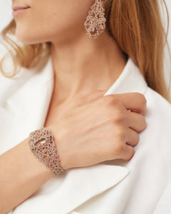 Gold lace earrings with intricate silk detailing and crystal accents, set against white fabric.