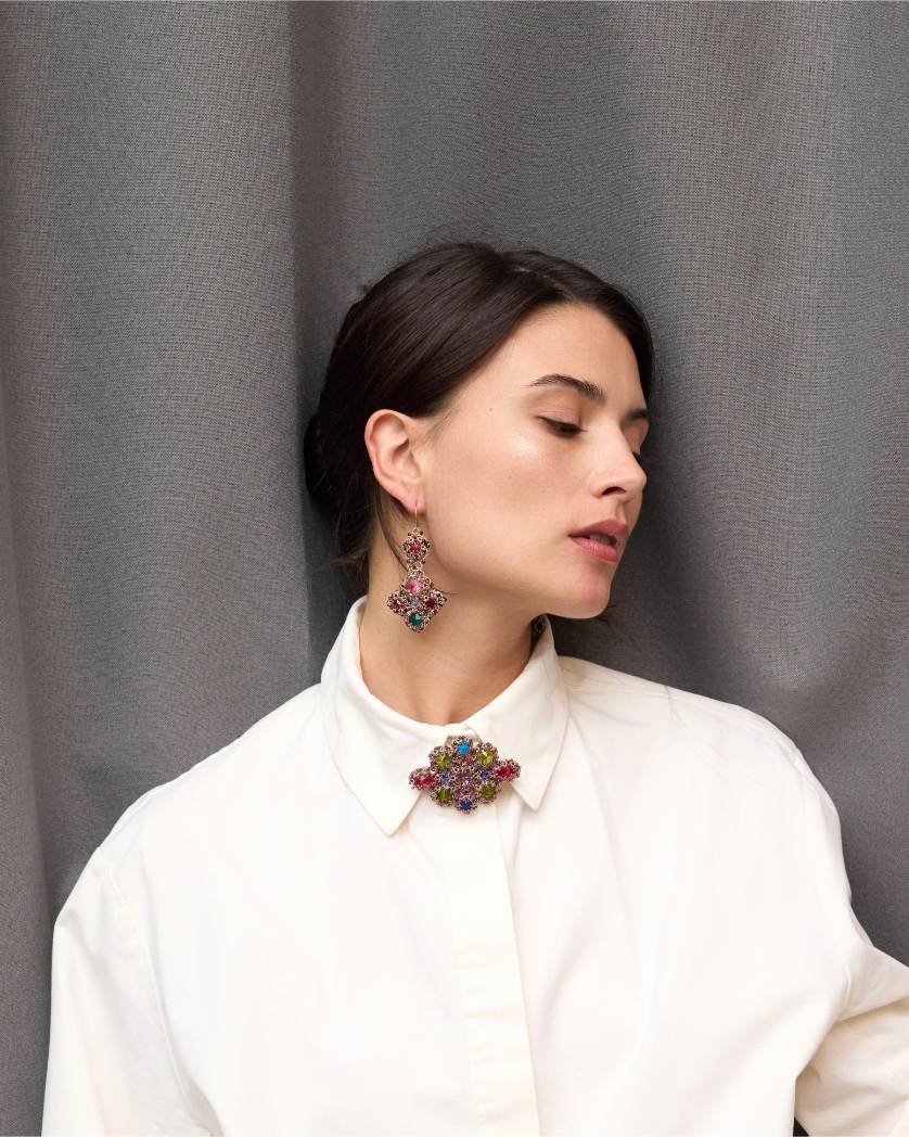 Woman wearing colorful silk earrings and matching brooch, set against a gray textured background.