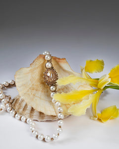 Gold-shayla pendant with pearls, intricate gold pendant design, side view against shell and yellow flower backdrop.