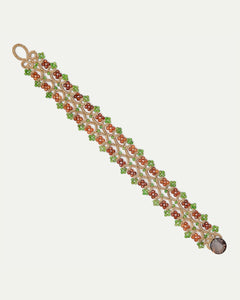 Green silk bracelet with pearl and garnet detailing, intricate floral design, woven texture visible.